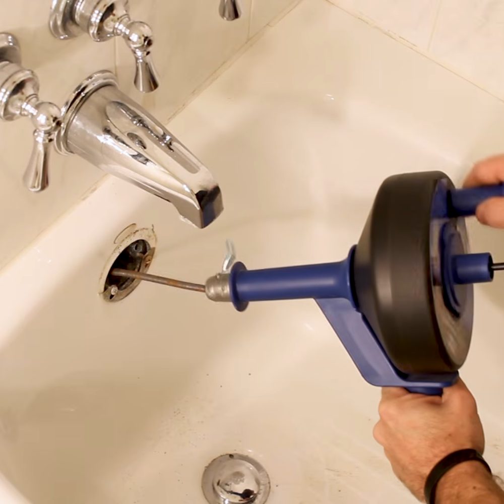 Drain auger cable fed through a bathtub overflow to clear a tub drain clog